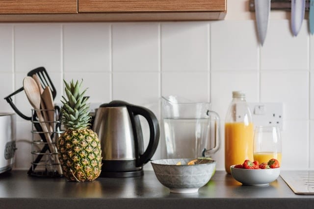 Kettle on a crowded worktop in the kitchen with fresh juice and a bowl of strawberries