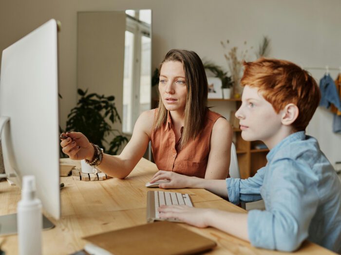 A woman and a boy sitting looking at a computer together