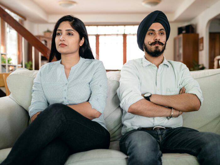 A man and a woman sitting on the sofa with folded arms looking cross with each other