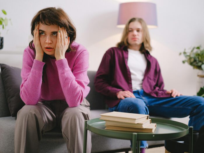 Woman and man sitting on the sofa. Woman looks distressed with her head in her hands