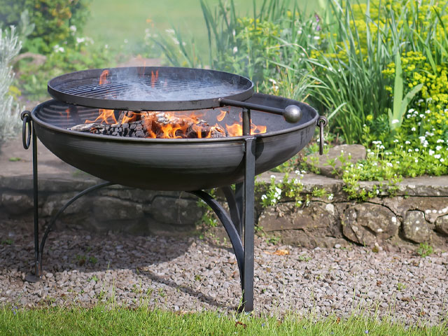 fire pit that can also be used to bbq on a patio by a green garden